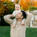 Man carrying a baby on his shoulders with autumn foliage in the background